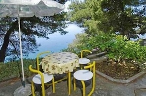 A table and chairs set outdoors with a view of a body of water and greenery. - Apartments Edo (Blato)