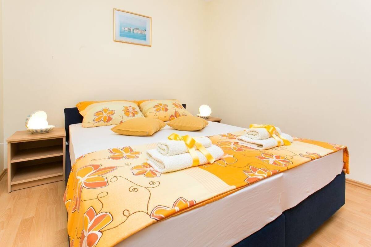Cama bem arrumada com roupa de cama floral, duas luminárias de cabeceira e uma pequena mesa de cabeceira com abajur.