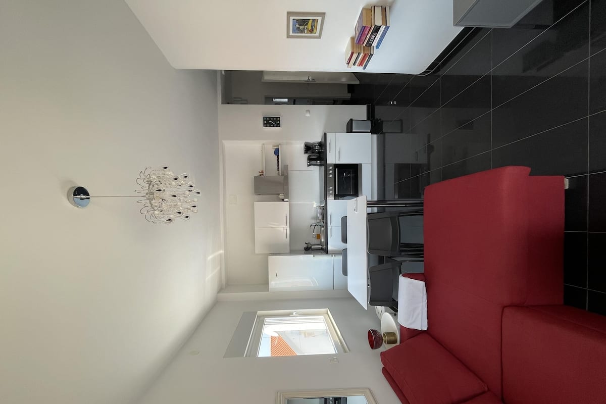A modern kitchen with white cabinets, a red sofa, and a small window.