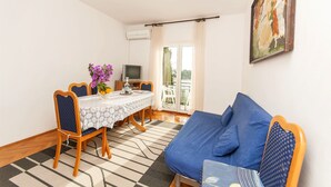 Une pièce comprenant une table à manger, des chaises, un canapé, un téléviseur et un balcon avec des rideaux.
