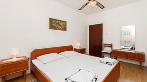 Une chambre à coucher avec un lit en bois, une table de chevet avec une lampe, un bureau en bois, une chaise, une armoire et un ventilateur de plafond.
