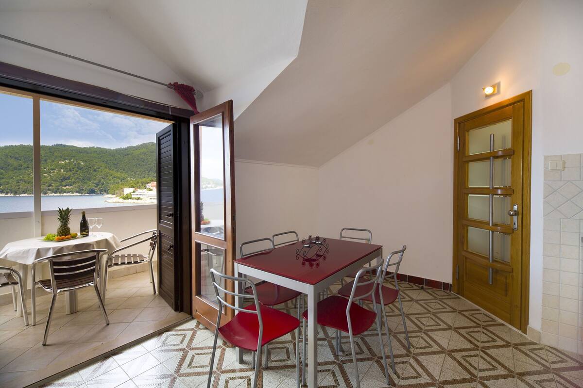 Un comedor con una mesa y sillas, vista al mar y una puerta con ventanal.