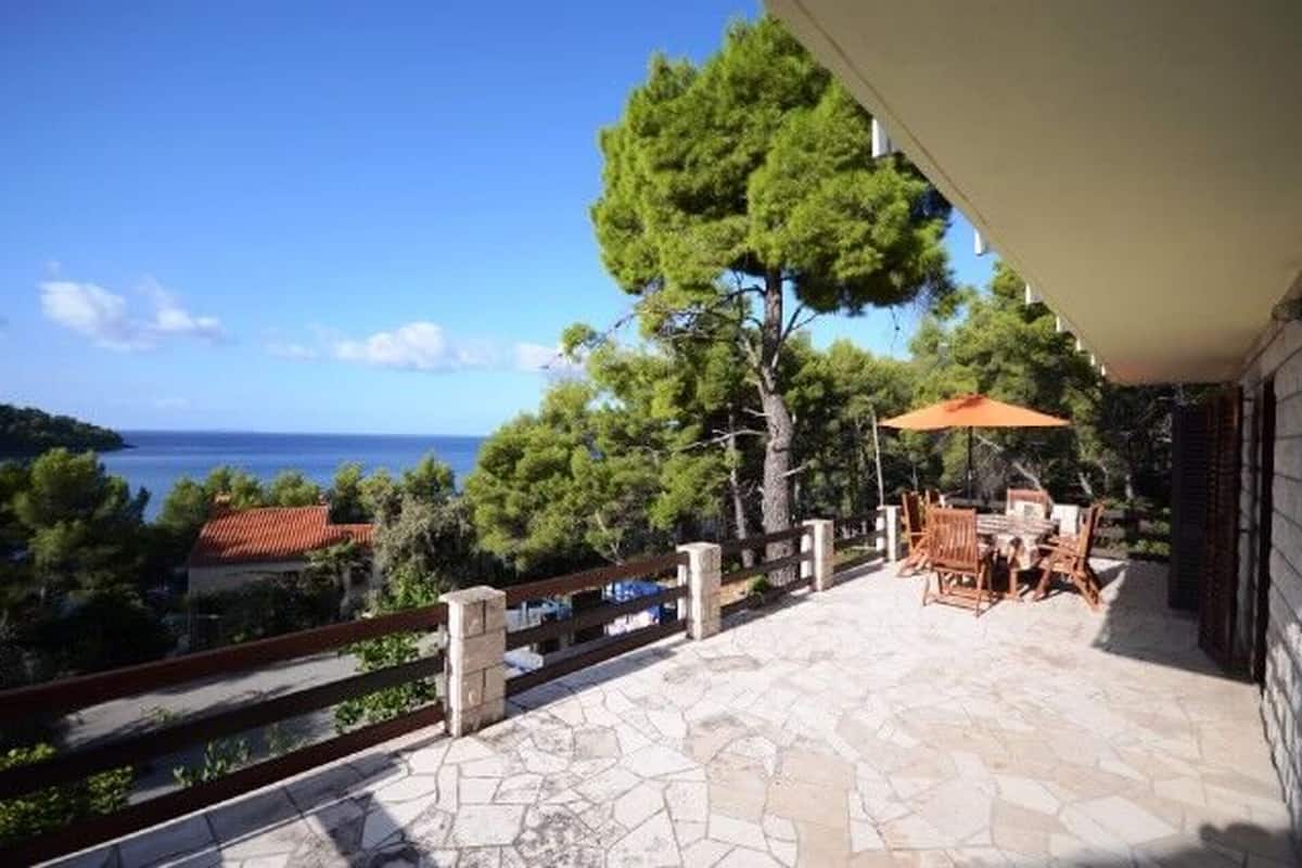 A terrace with stone flooring, a wooden fence, and a table with chairs under an umbrella.