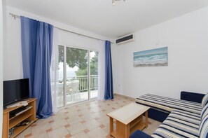 A living room with a sofa, a TV, a table, and a balcony with curtains. - Apartments Marjan (Smokvica)