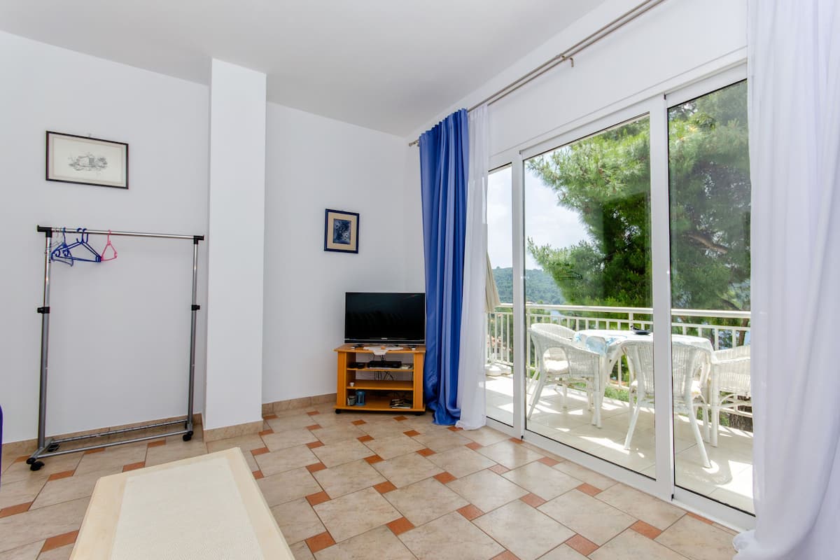 A room with a TV, a clothing rack, and a balcony with outdoor furniture.