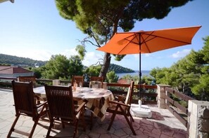 An outdoor patio with a table and chairs, an orange umbrella, and a scenic view of a lake and hills. - Apartments Marjan (Brna)