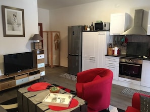 A compact living space with a TV, red armchair, kitchenette, and a dining area with a table and red placemats.
