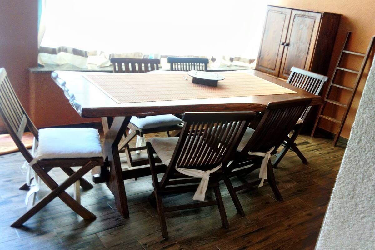 A dining area with a wooden table and chairs, a window with curtains, and a wooden cabinet.