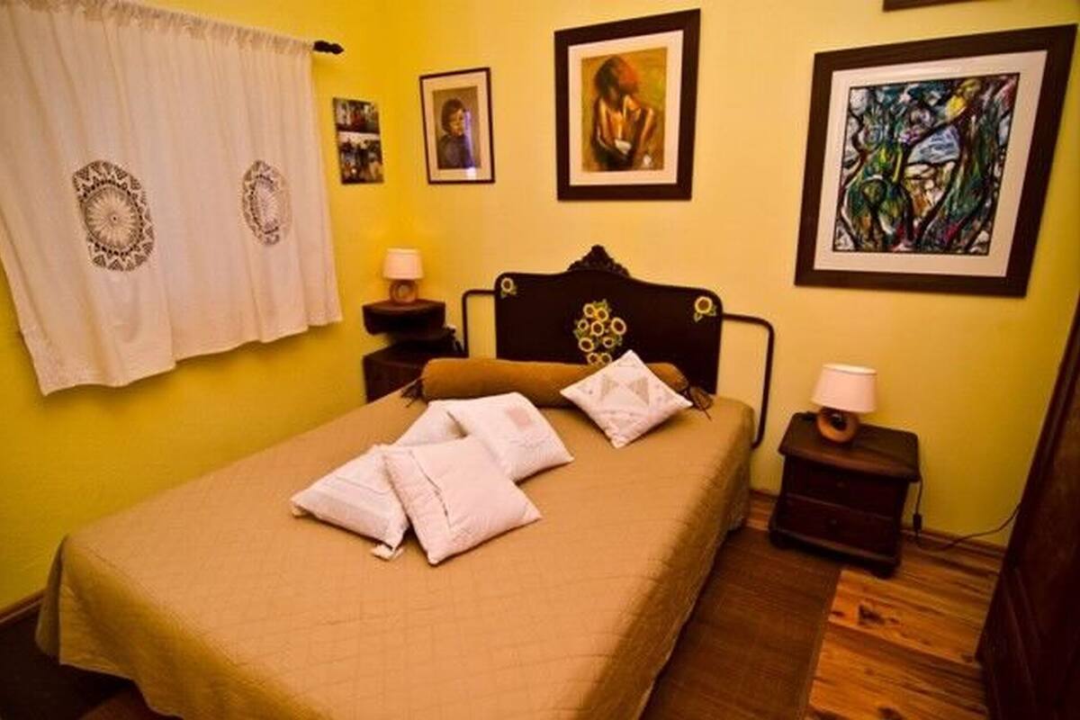 A hotel room with a bed, two bedside tables, a nightstand, a lamp, and artwork on the walls.