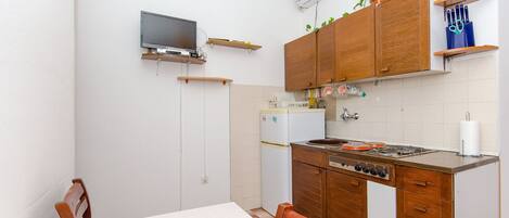 Una cocina compacta con armarios de madera, una estufa integrada, un refrigerador y un televisor montado en la pared.