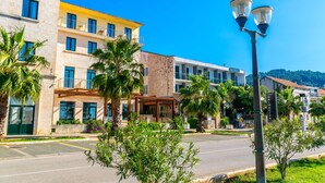Un hôtel à plusieurs étages, doté d’une façade jaune, d’un espace extérieur aménagé avec des sièges et abrité, et situé dans une rue bordée de palmiers.