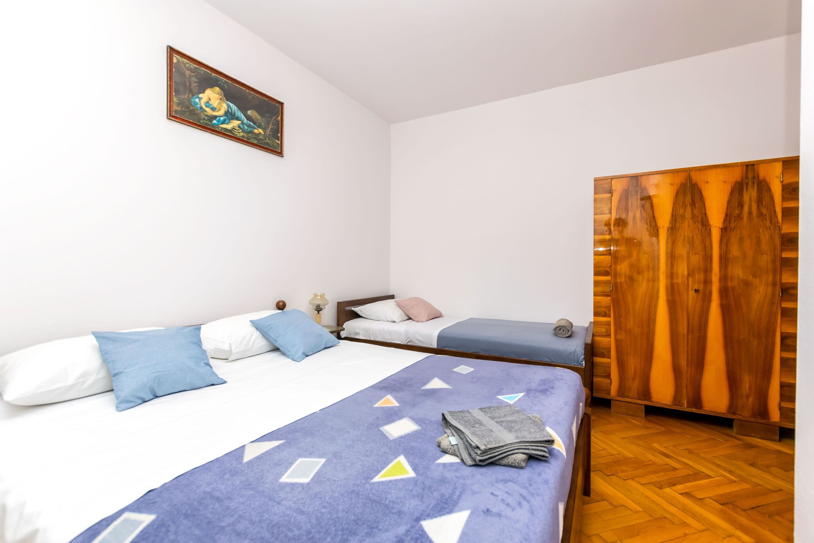 Una habitación con dos camas, un armario de madera y un cuadro en la pared.