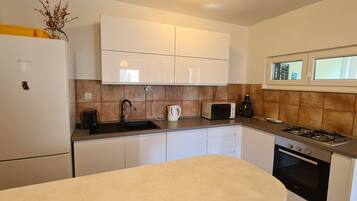 A compact kitchen with a Bosch refrigerator, white cabinets, a sink, a microwave, a gas stove, and a window above the sink.