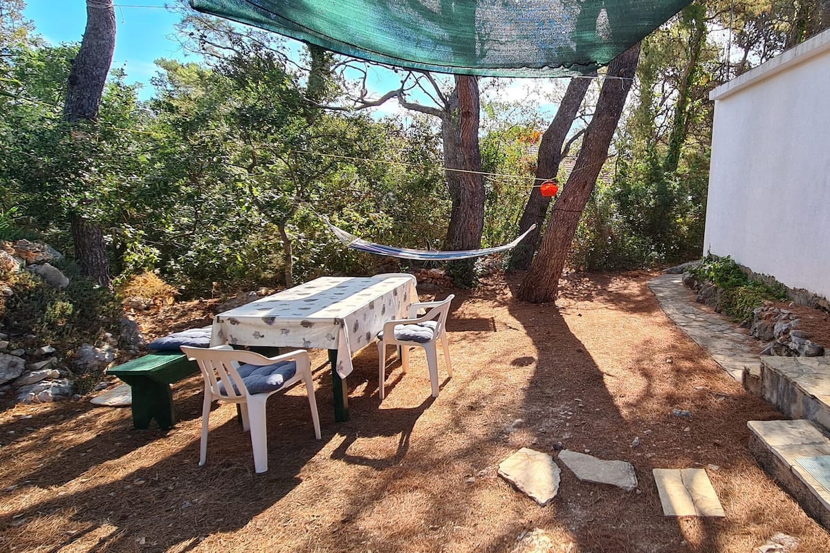 A patio area with a table and chairs, a hammock, and a stone pathway leading to a building with a green shutter.