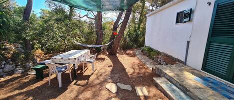A patio area with a table and chairs, a hammock, and a stone pathway leading to a building with a green shutter.