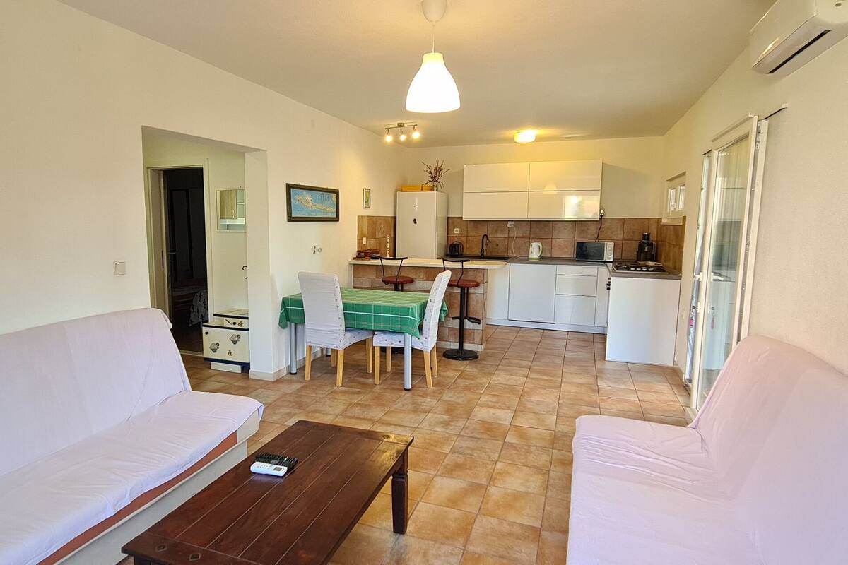 A living room with a sofa, a coffee table, and a dining area with a table and chairs. There is a kitchen area with cabinets and a refrigerator.