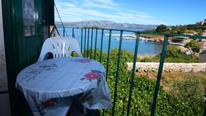 A balcony with a table and chairs, overlooking a coastal area with boats and a mountainous backdrop. - Apartments Loredana (Lumbarda)
