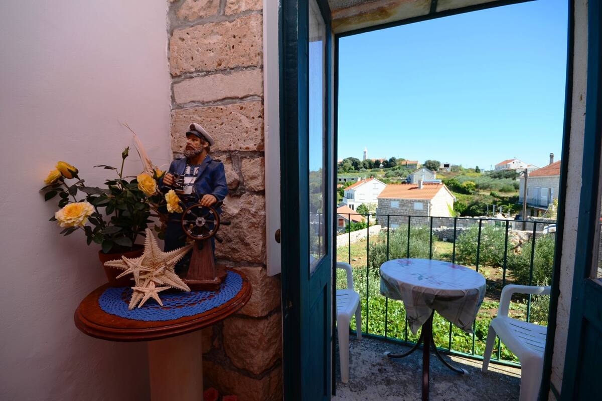 Un balcon donnant sur des maisons, une statue et une table avec une chaise.