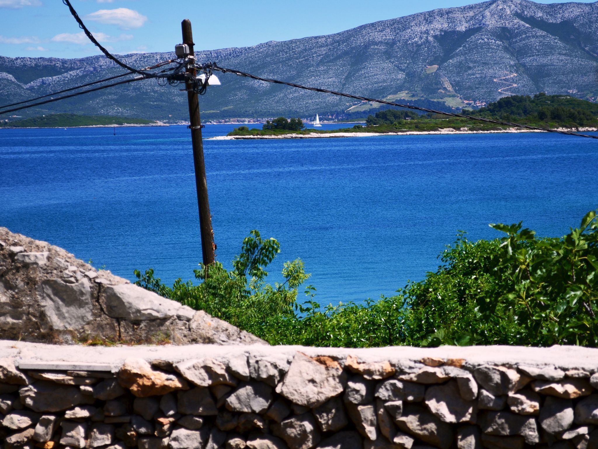 A stone wall with a view of a calm sea and distant mountains.