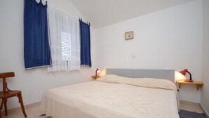 A bedroom with a bed, two bedside lamps, a chair, and a window with curtains. - Apartments Loredana (Lumbarda)