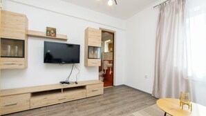 A modern living room with a flat-screen TV, wooden furniture, a small table, and a window with curtains. - Apartment Ivan (Lumbarda)