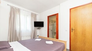 A hotel room with a bed, a TV, a shower, and a wooden door. - Apartment Ivan (Lumbarda)