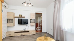 A modern living room with a flat-screen TV, wooden furniture, a round coffee table, and a large window with curtains. - Apartment Ivan (Lumbarda)
