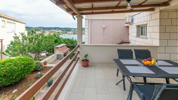 A balcony with a table and chairs, potted plants, and a view of the surrounding area. - Apartment Ivan (Lumbarda)