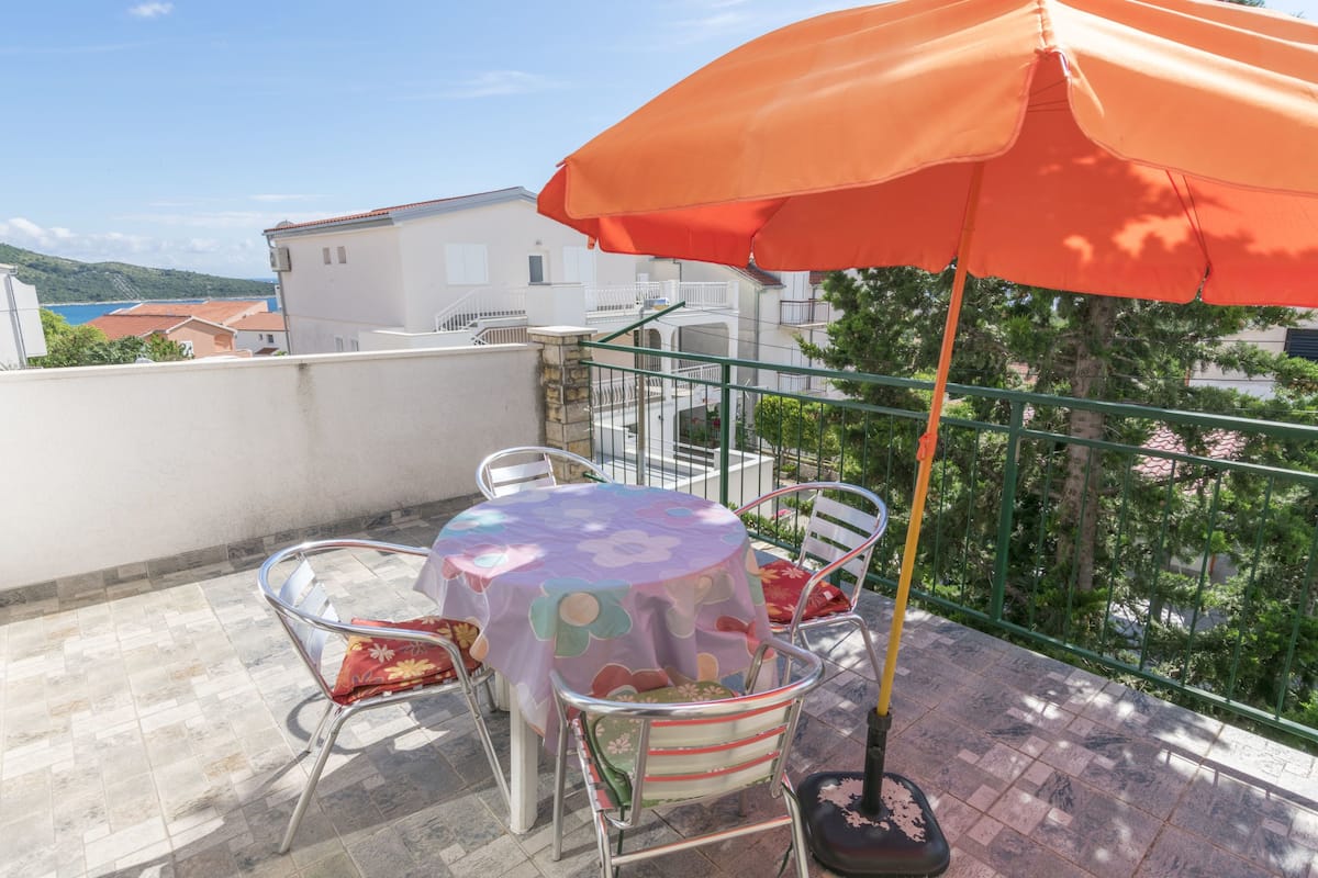 A balcony with a round table, chairs, and an orange umbrella.