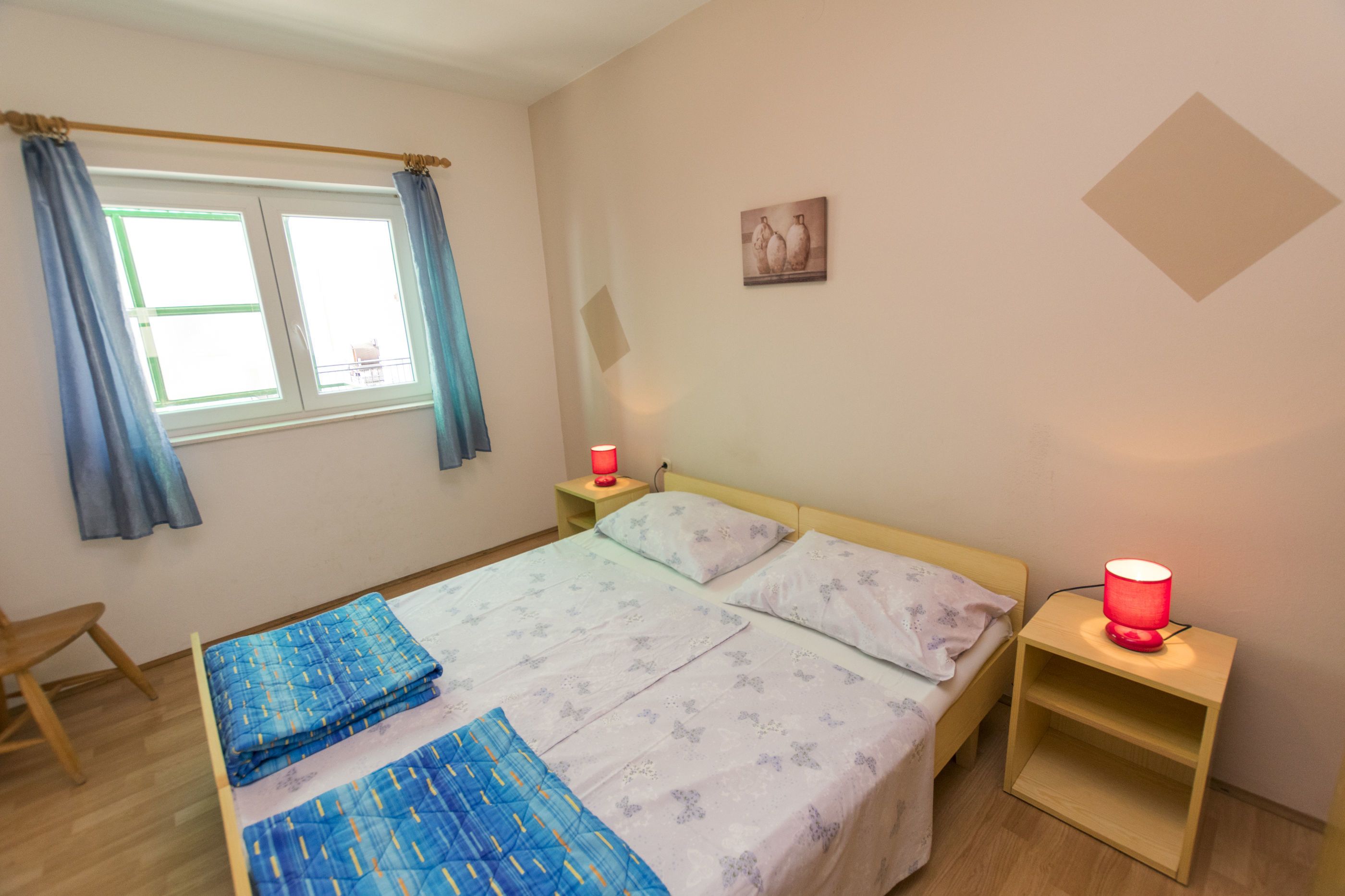 A bedroom with a bed, two bedside tables, a nightstand, a window with curtains, and a wall-mounted picture.