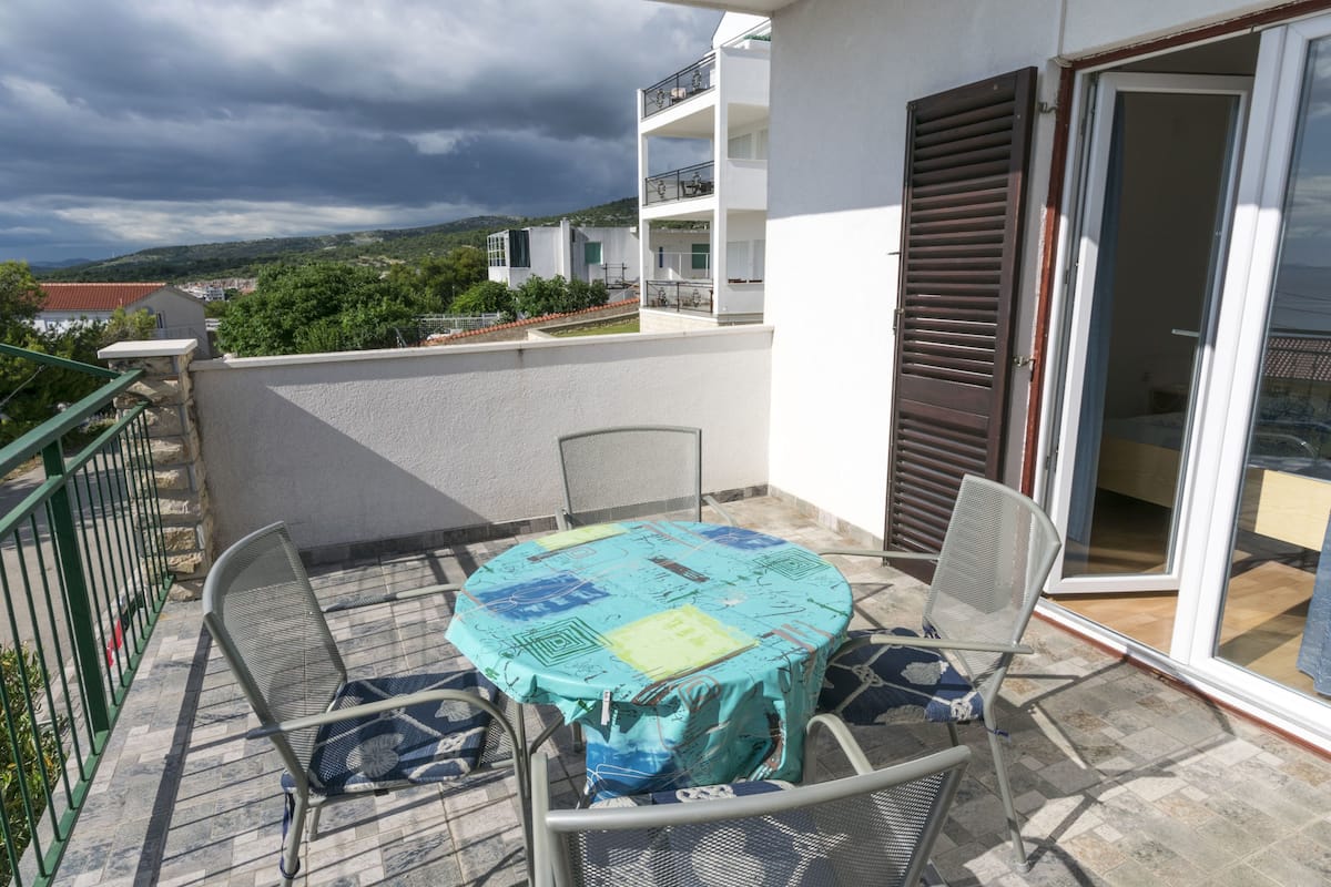 A balcony with a table and chairs, a sliding glass door, and a view of a building and landscape.