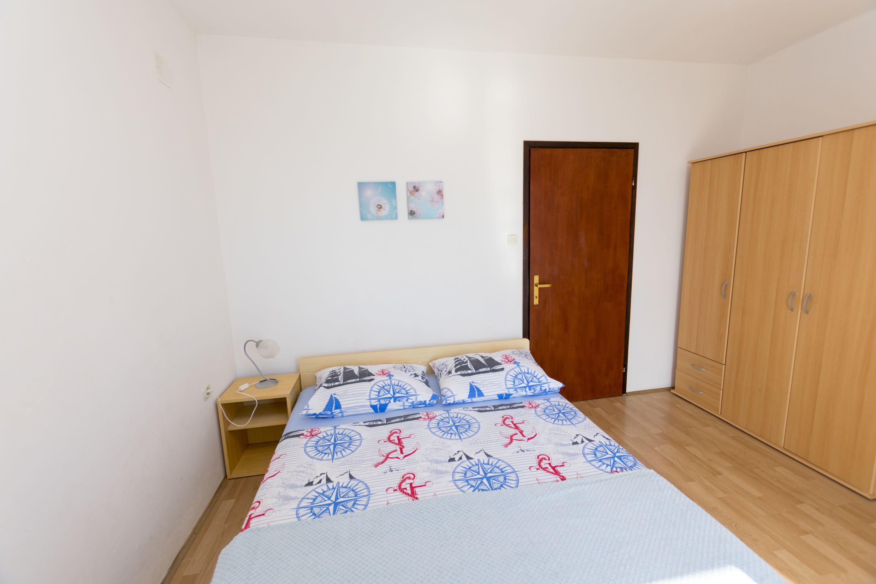 A bedroom with a bed, wooden wardrobe, and a nightstand with a lamp.
