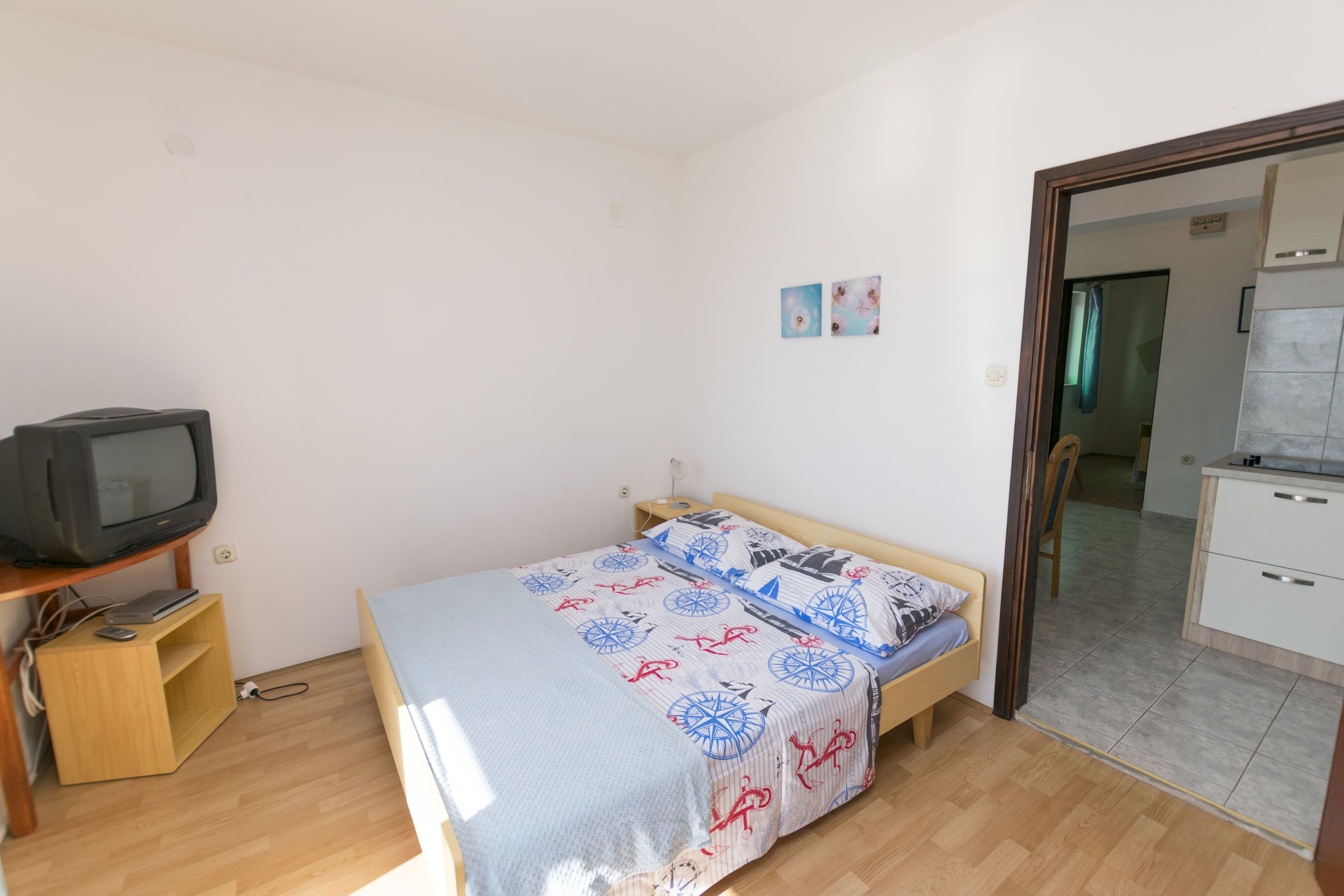 A small, sparsely furnished room with a bed, a television, and a wooden cabinet.