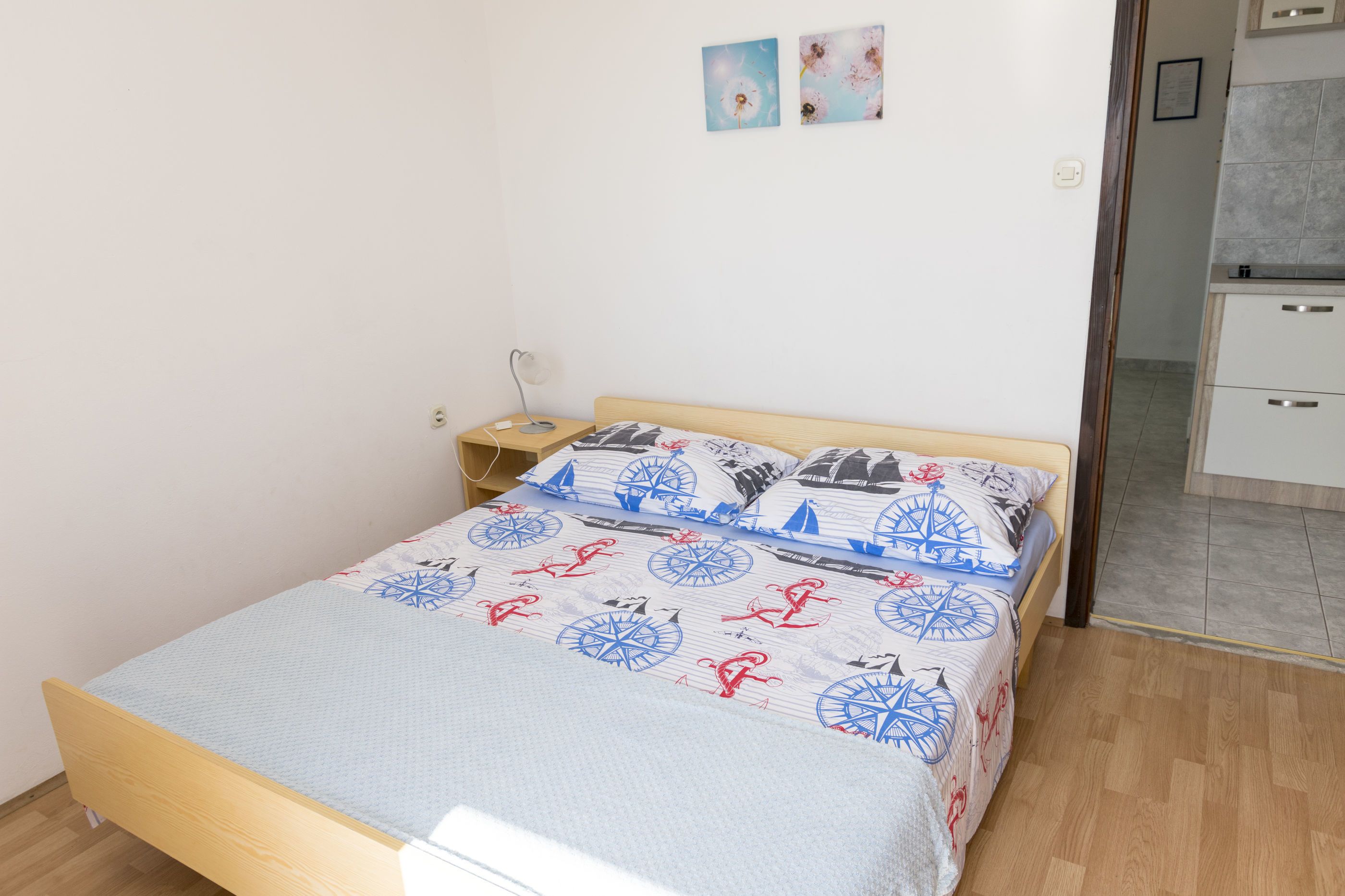 A bedroom with a bed, a nightstand, a wall-mounted lamp, and a small cabinet.