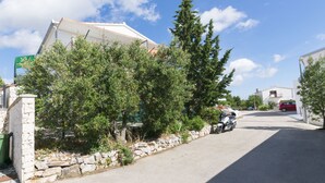 A residential street with a stone wall, trees, and a parked scooter. - Apartments Ksenija (Primosten)