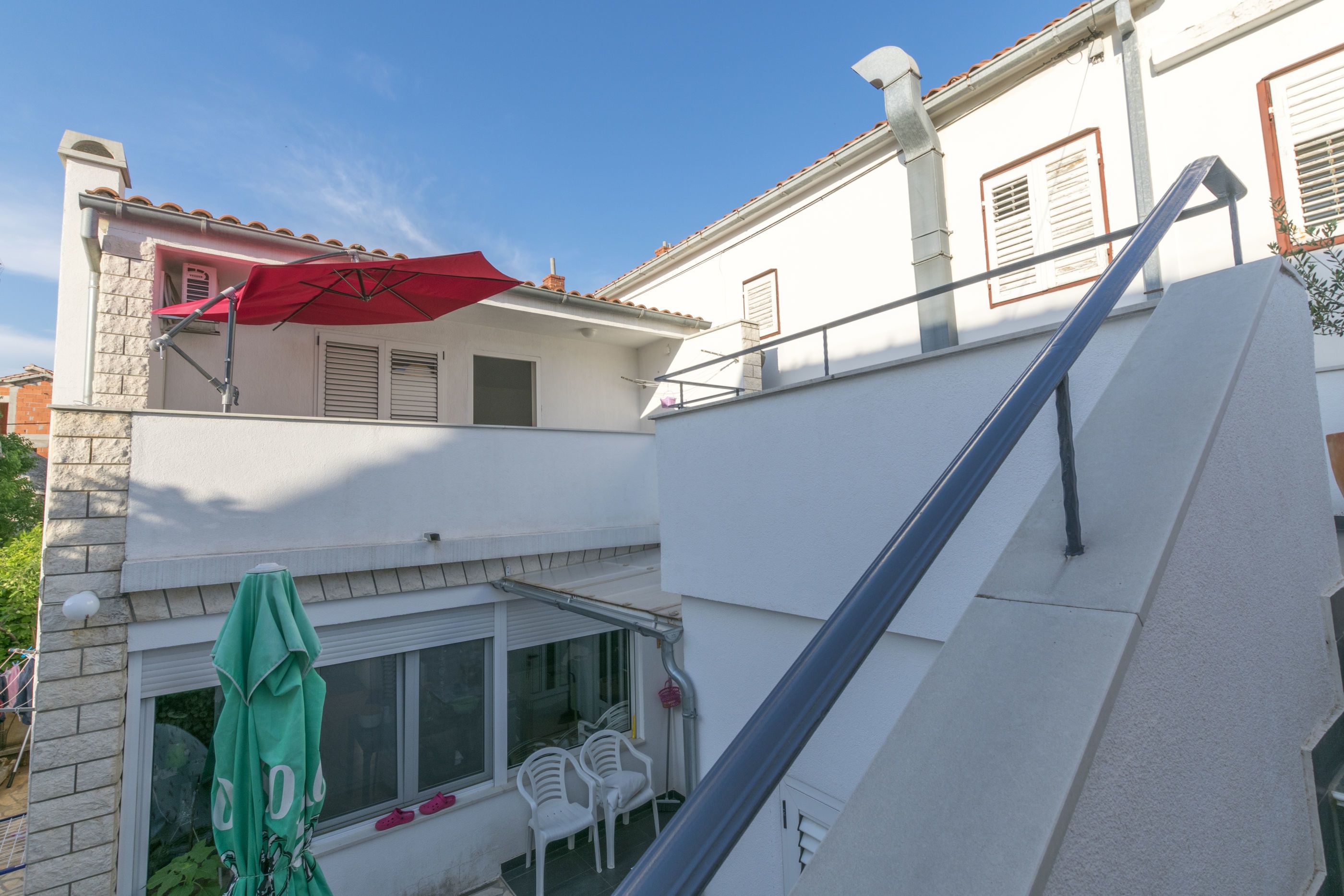 A two-story building with a balcony, white walls, and a red umbrella.