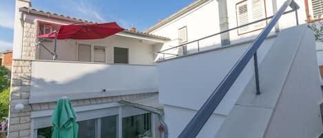 A two-story building with a balcony, white walls, and a red umbrella.