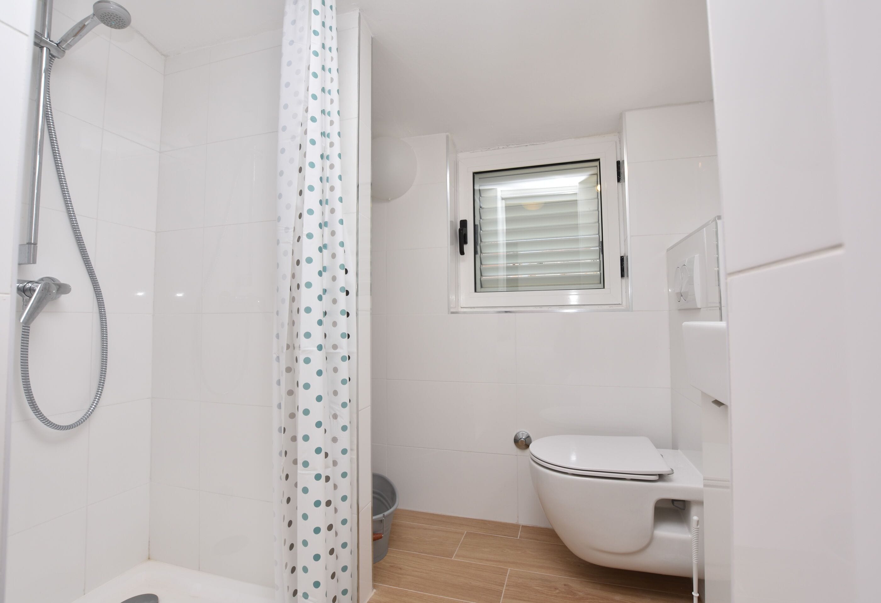Un baño con ducha, inodoro y ventana con persianas.