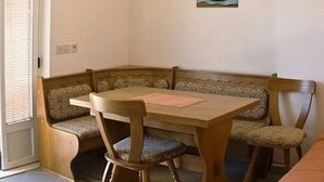 Eine Essecke mit einem Holztisch und vier Stühlen, einer Bank mit gemusterten Kissen und einem kleinen Tisch mit Platzdeckchen.