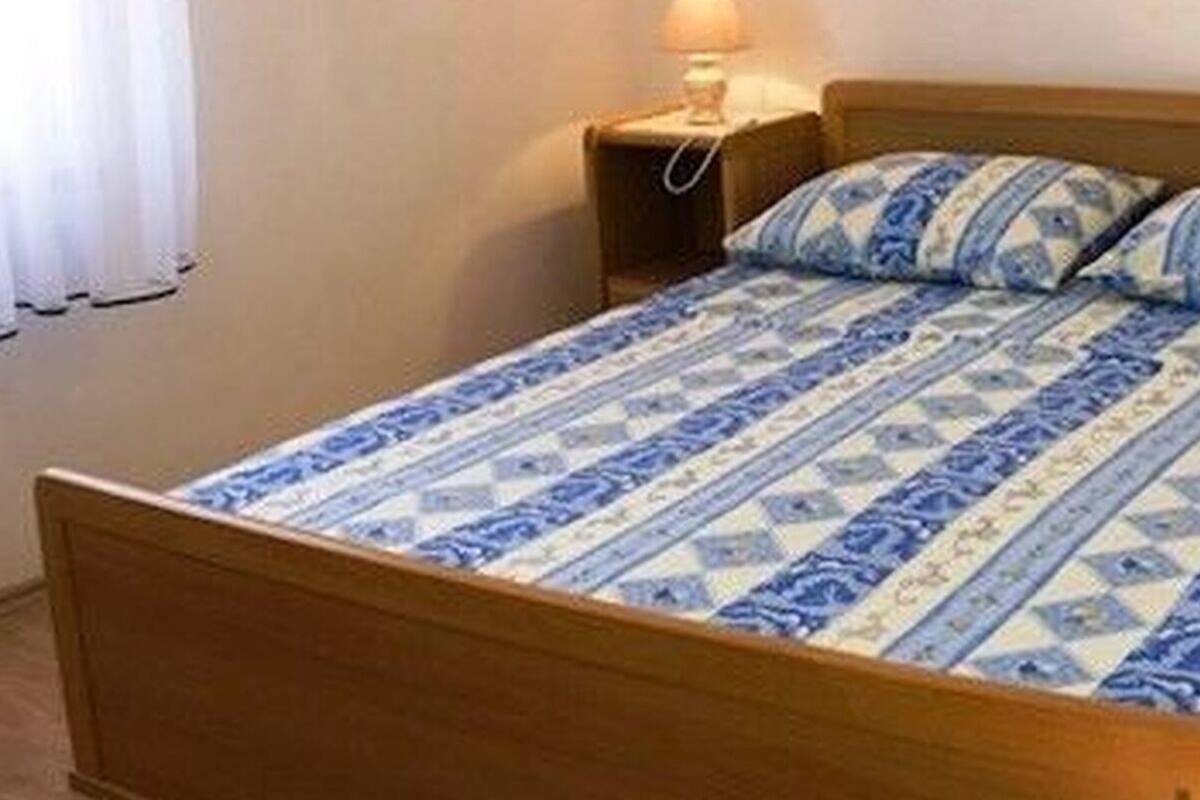 A single bed with a patterned bedspread and matching pillows, a wooden headboard, and a nightstand with a lamp.