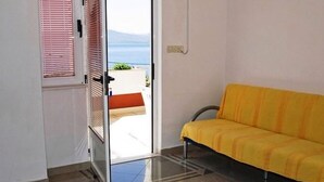 Ein Zimmer mit gelbem Sofa, einer Schiebetür zum Balkon und Blick auf das Meer.