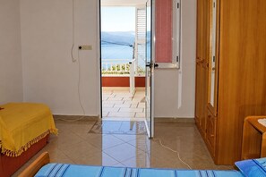 A room with a bed, a wooden door, and a view of a balcony with a railing.