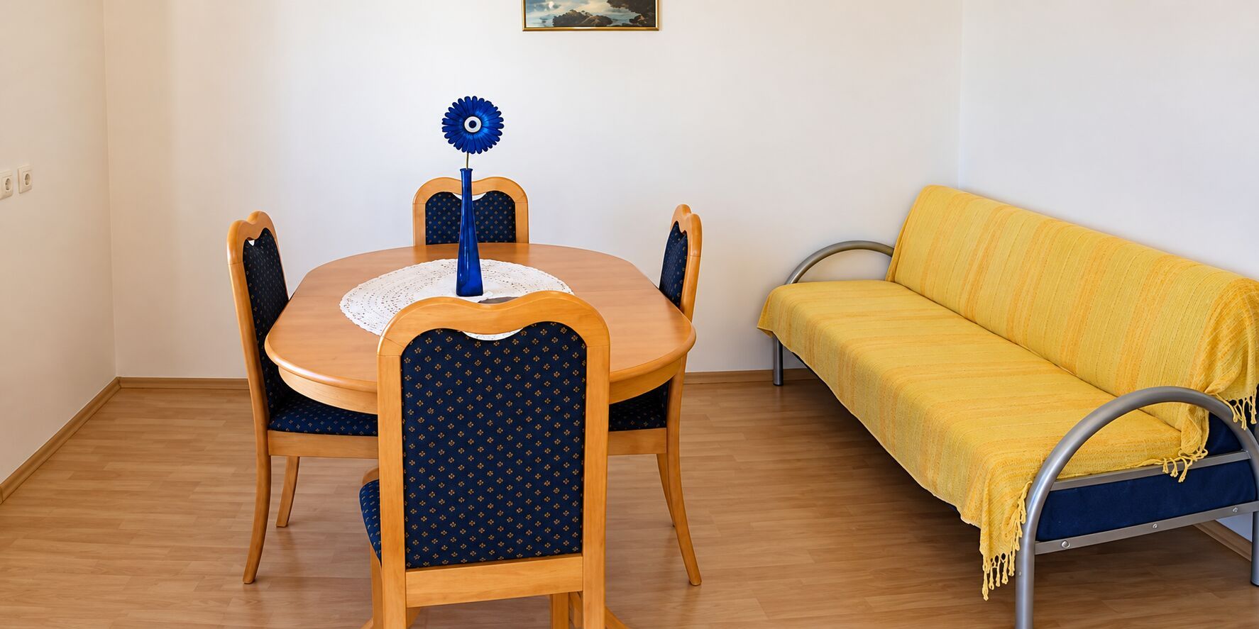 En matplats med ett runt träbord, fyra stolar med mörkblått tyg och en gul soffa med metallram.