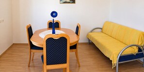A dining area with a round wooden table, four chairs with dark blue upholstery, and a yellow sofa with a metal frame. - Apartments and Rooms Florijan (Komarna)