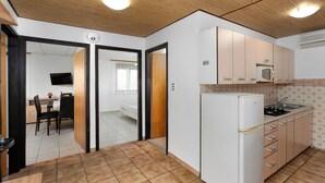 A compact kitchen with a refrigerator, microwave, and sink. There is a dining area with a table and chairs visible through an open door. - Apartments Kralj (Privlaka)