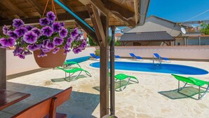 A pool area with lounge chairs and a hanging flower basket. - Apartments Kralj (Privlaka)