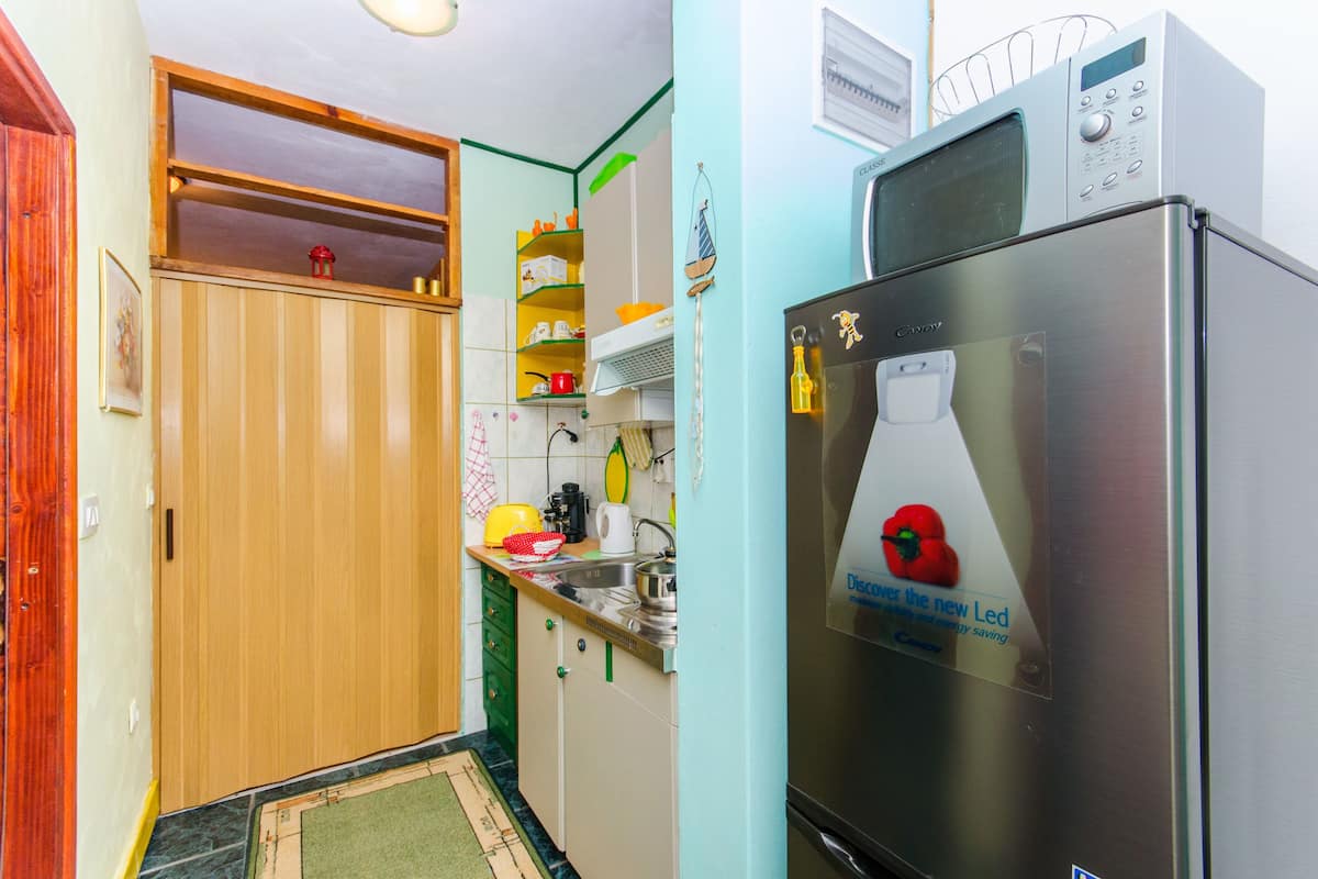 A compact kitchen with a stainless steel refrigerator, wooden cabinets, and a microwave on top.