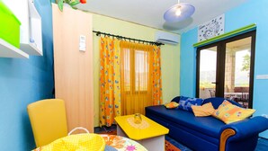 A room with a blue sofa, yellow and orange curtains, a small table with a yellow lamp, and a colorful rug. - Apartment Slavka (Kneza)