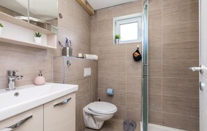 Features a sleek bathroom with a large mirror, white toilet, and glass-enclosed shower.