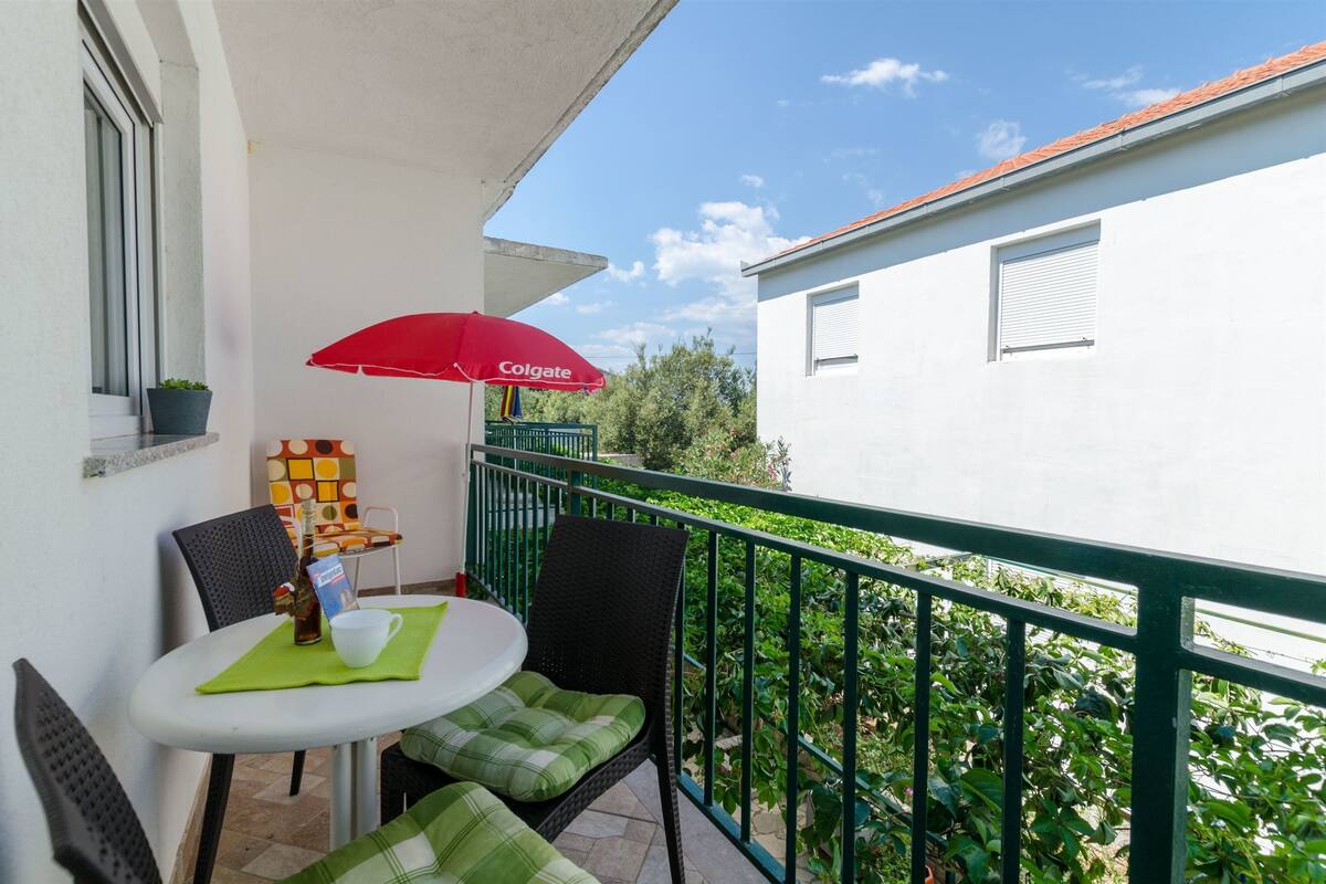 Ein Balkon mit Tisch, Stühlen, einem roten Sonnenschirm und einem Blumentopf.